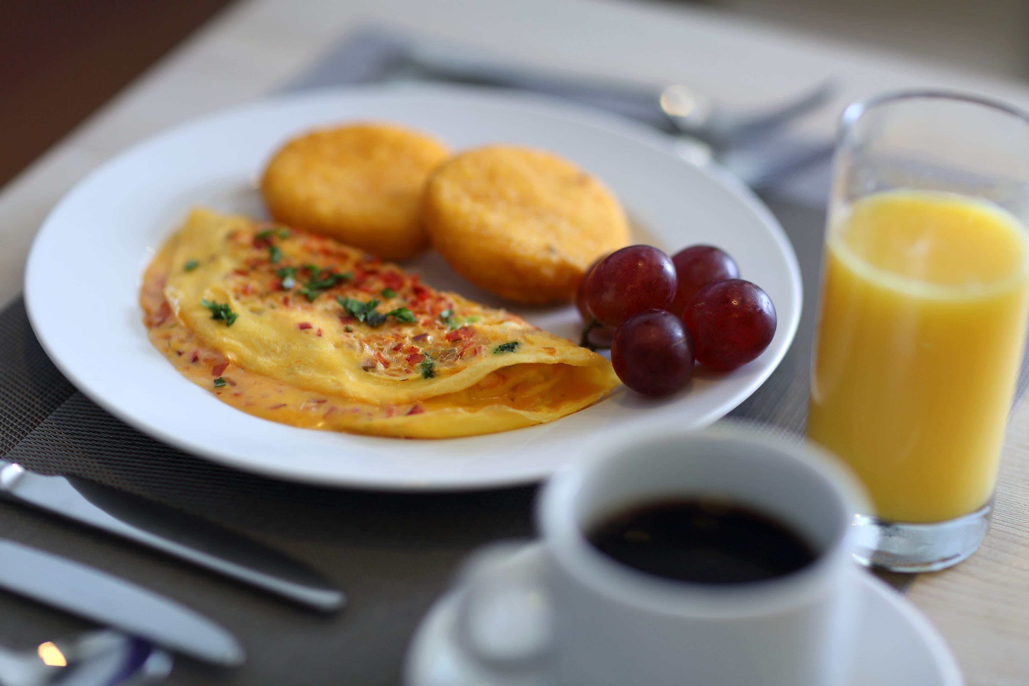 Un plato de desayuno con tortilla, dos galletas y uvas, acompañado de un vaso de jugo de naranja y una taza de café.