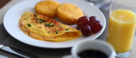 Un plato de desayuno con tortilla, dos galletas y uvas, acompañado de un vaso de jugo de naranja y una taza de café.