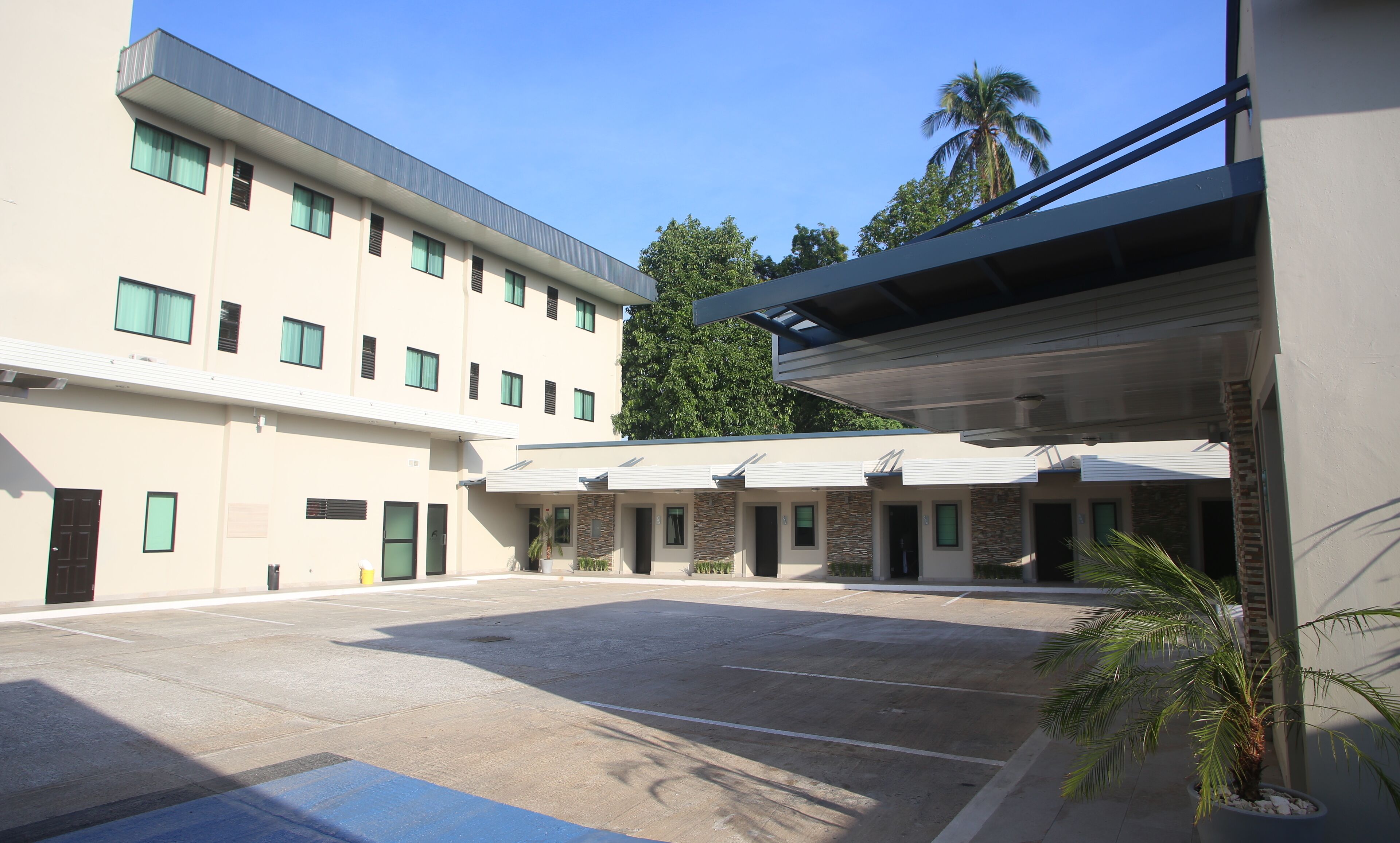 A multi-story hotel with a parking lot, a covered walkway, and a palm tree.