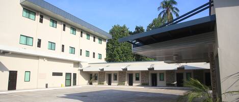 A multi-story hotel with a parking lot, a covered walkway, and a palm tree.