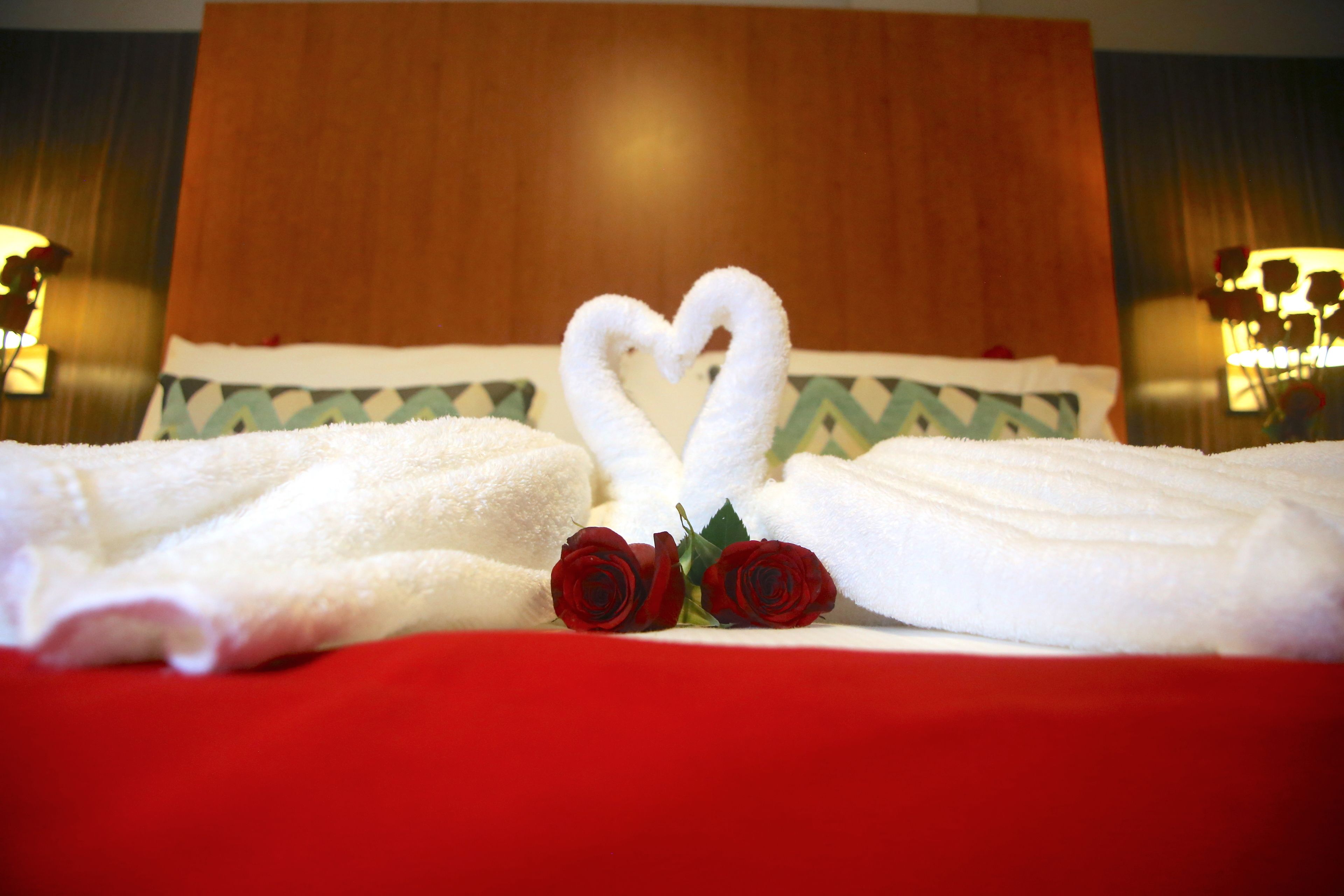 Una cama con toallas blancas y dos rosas rojas dispuestas en forma de corazón.
