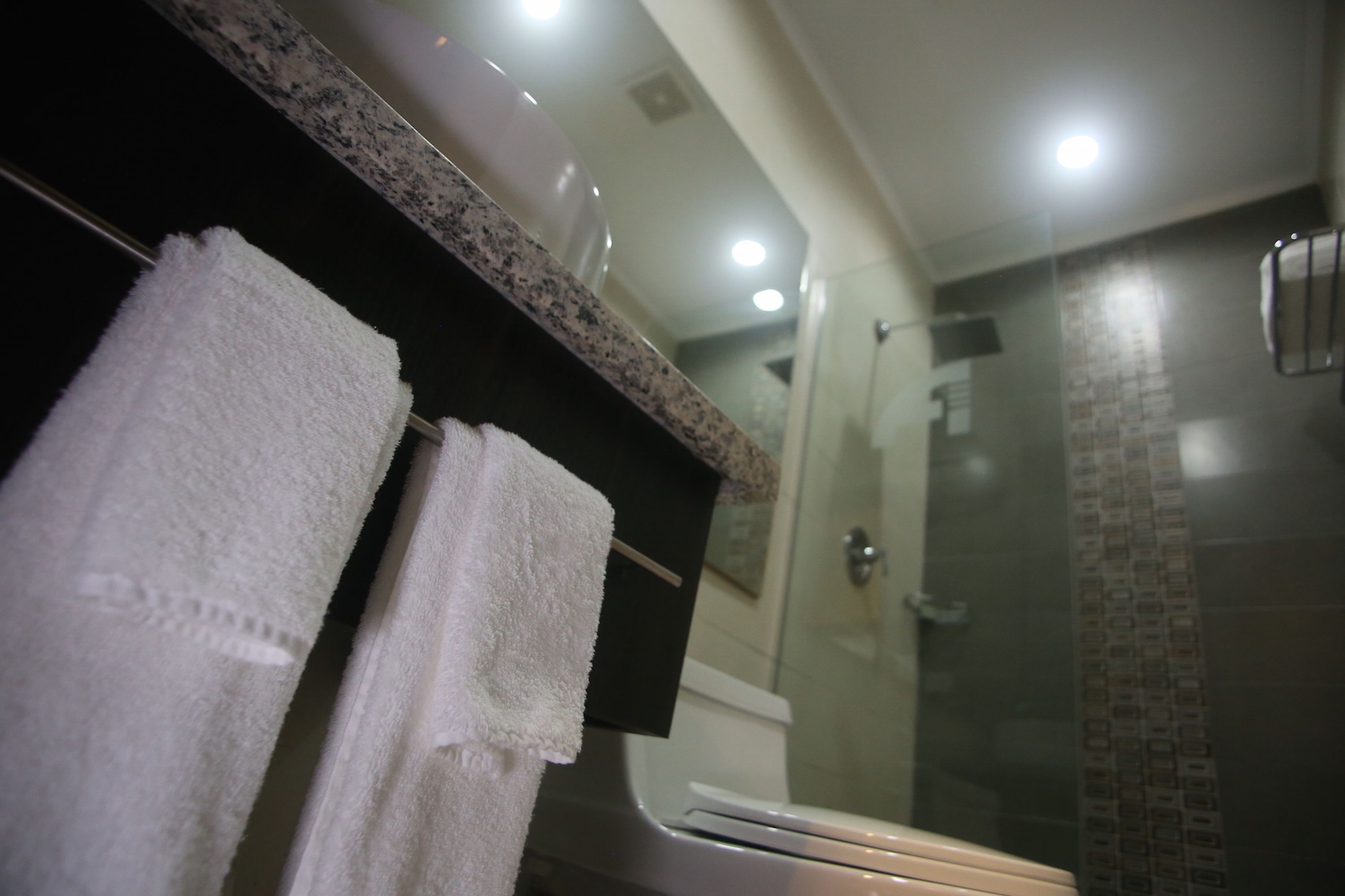 A bathroom with a granite countertop, two white towels, a mirror, and a glass shower enclosure.