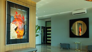 Un interior moderno con un cuadro abstracto grande, un banco, un espejo redondo y una zona de estar con cojines.