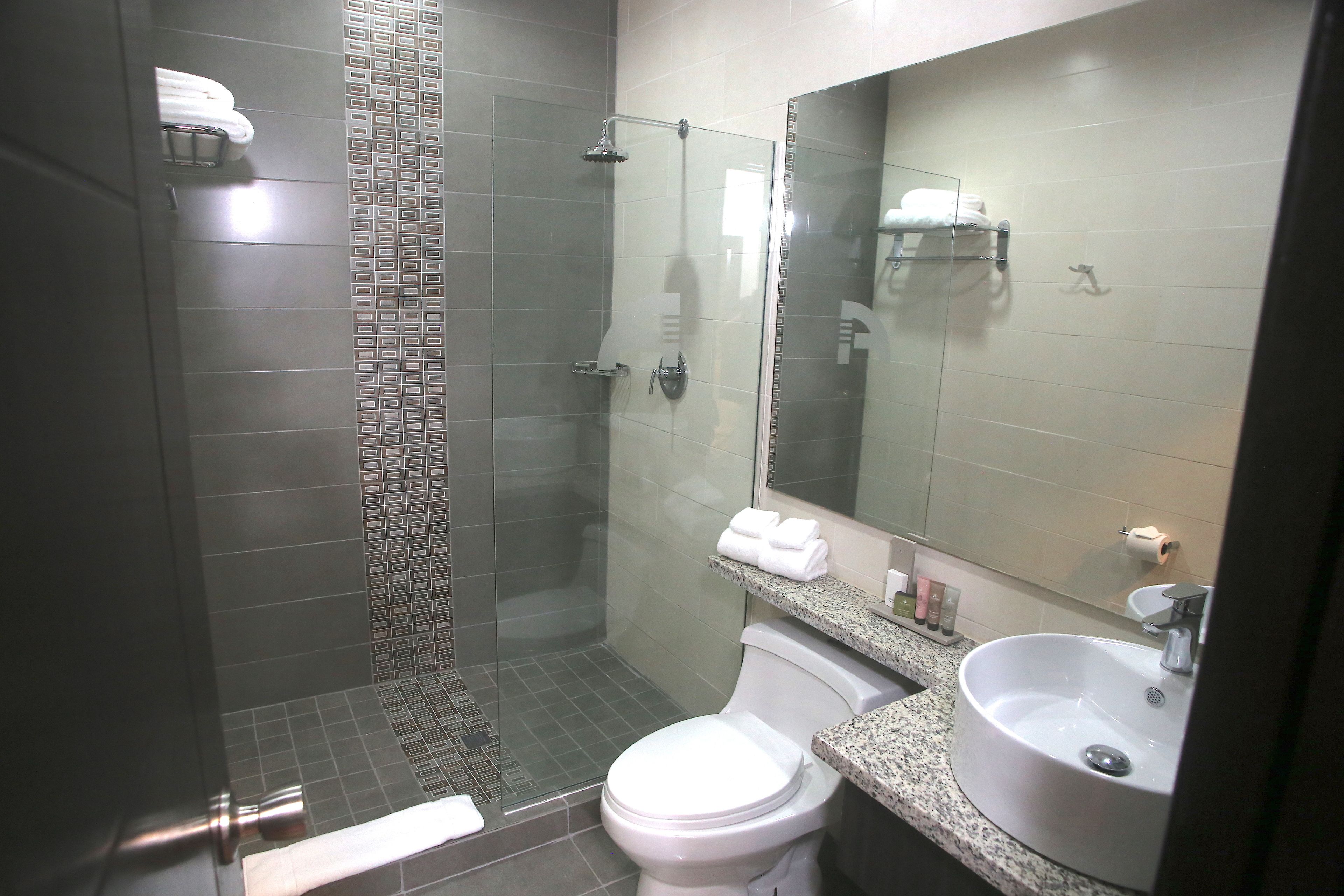 Ein modernes Badezimmer mit einer gläsernen Duschkabine, einer weißen Toilette, einem Waschbecken mit Spiegel und einem Handtuchhalter mit Handtüchern.