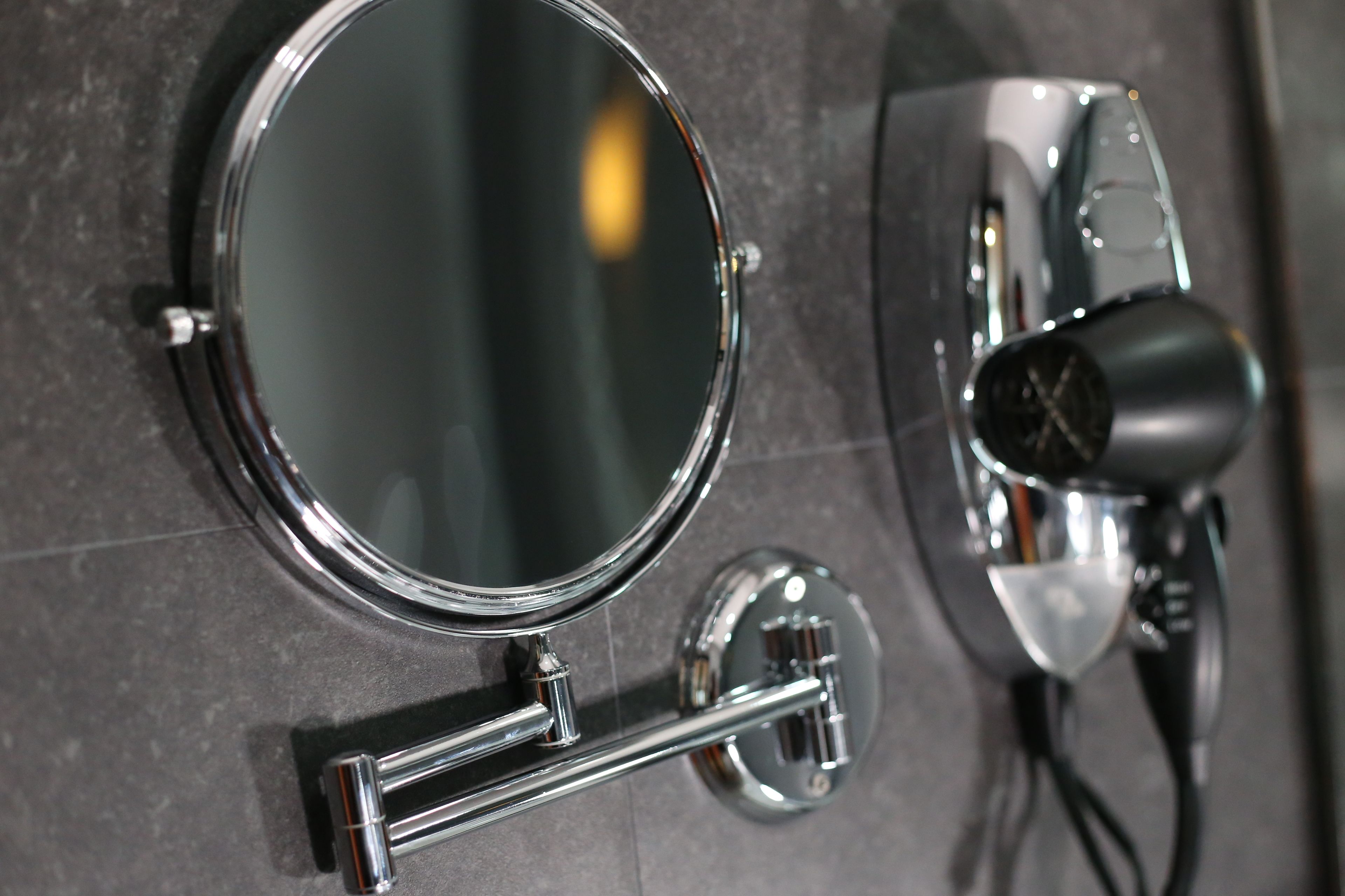 A bathroom mirror with a chrome frame and a hairdryer mounted on the wall.