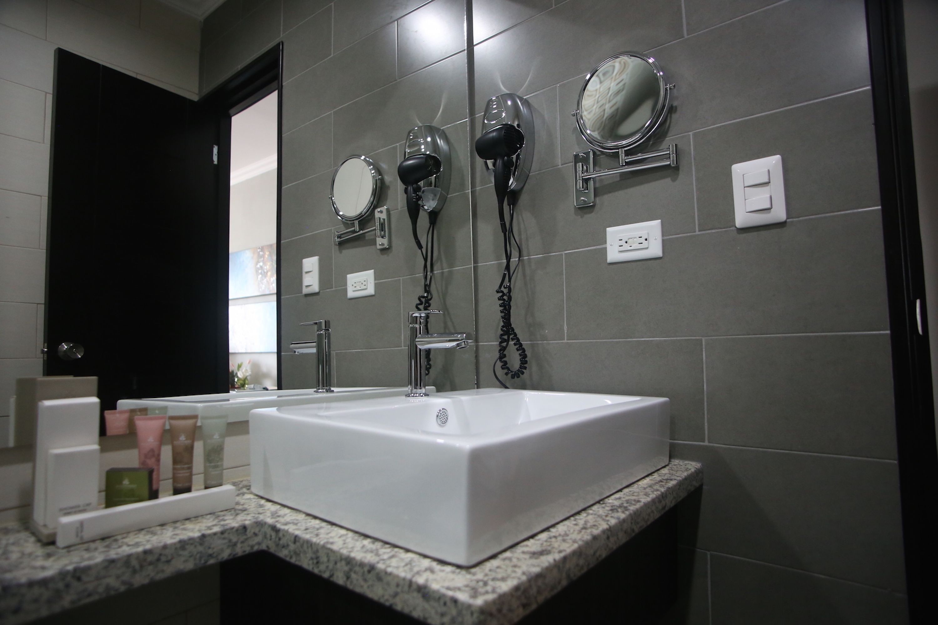 A bathroom with a white sink, two hair dryers mounted on the wall, and a mirror.