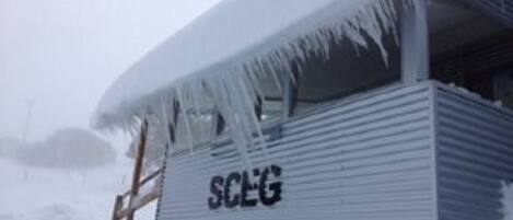 Un edificio de metal con la palabra "SCEG" en su lateral, parcialmente cubierto de nieve y hielo.