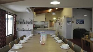 Un comedor con una mesa larga dispuesta para una comida, una cocina al fondo y un refrigerador a la derecha.