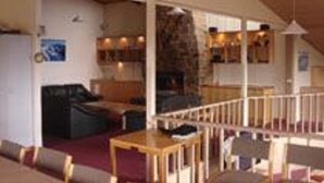 Un interior acogedor con techo de madera, una zona de estar con sofá y una mesa, y una cocina visible al fondo.