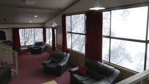 Una habitación con alfombra roja, sofás de cuero, una escalera de madera y ventanas grandes con cortinas.