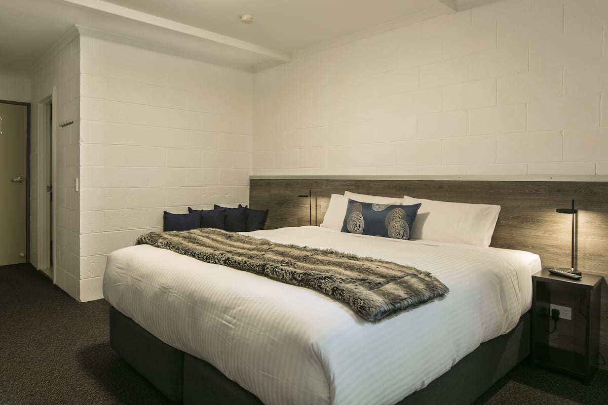 Quarto moderno com uma cama grande, cabeceira de madeira e mesa de cabeceira com abajur.