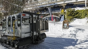 A snow-covered area with a bus and tracks, a building with balconies, and a sign for a ski resort. - Falls Creek Hotel (Falls Creek)