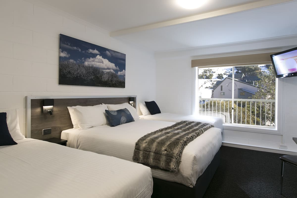 Quarto de hotel com duas camas, uma janela grande com vista, uma televisão montada e um quadro na parede.