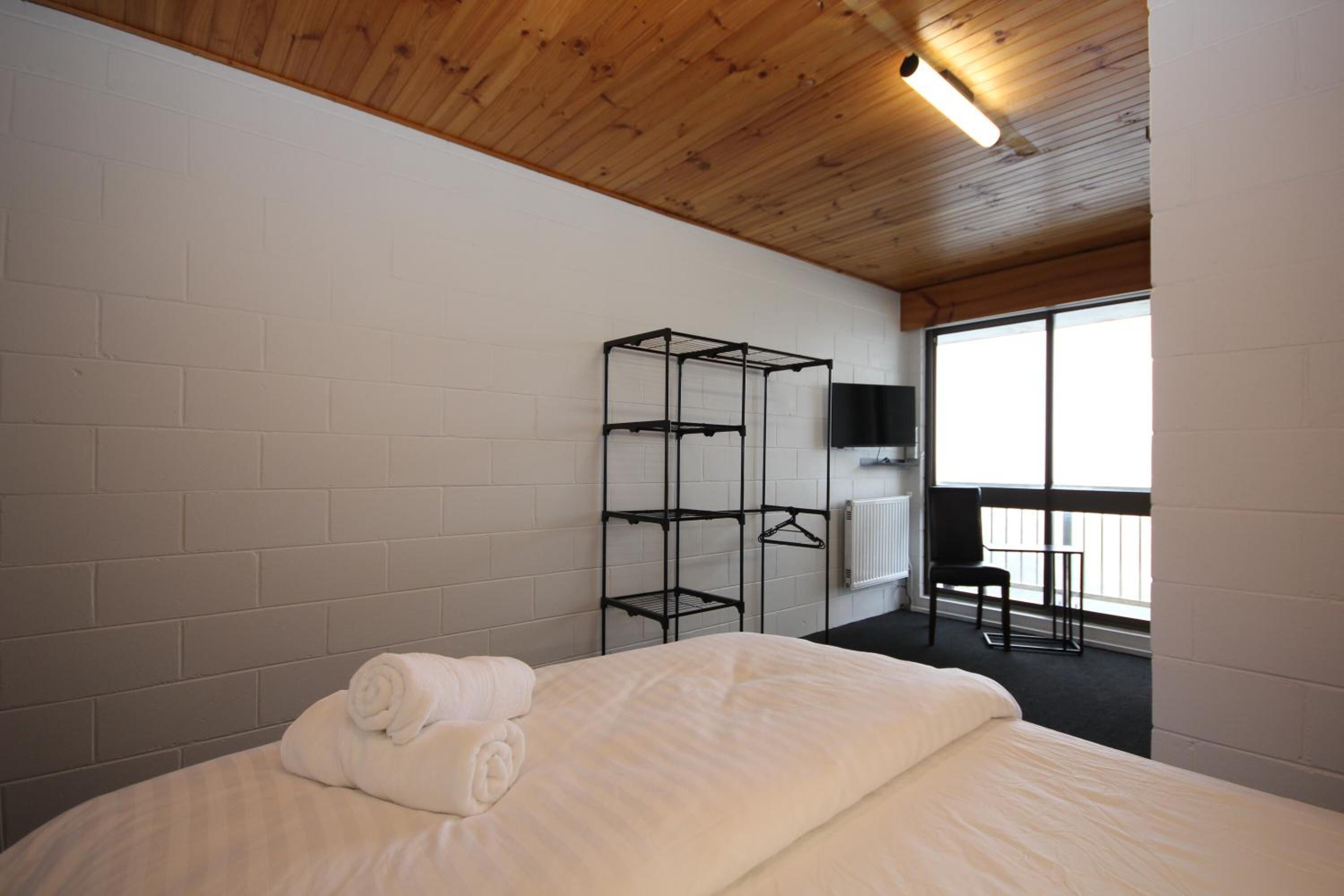 Une chambre d’hôtel avec un lit, une étagère en métal, une chaise et une fenêtre.