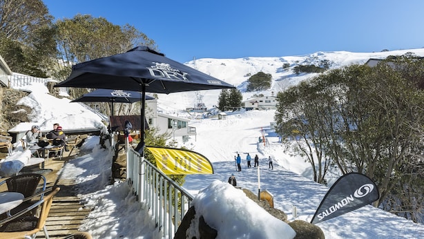 A ski resort with a covered seating area, a chairlift, and a snowy mountain backdrop. - Falls Creek Hotel (Falls Creek)