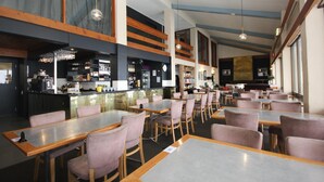 A restaurant with multiple tables and chairs, a bar area, and a counter with various items. - Falls Creek Hotel (Falls Creek)