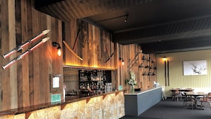 A bar area with a stone wall, wooden paneling, and a variety of bottles and glasses. - Falls Creek Hotel (Falls Creek)
