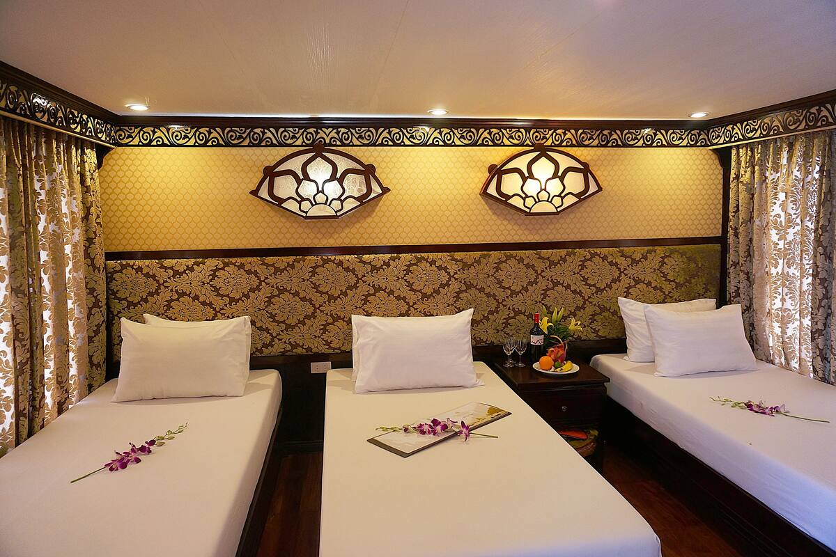 A hotel room with two beds, each with white linens and a single purple orchid. There are two wall sconces with a geometric design, and the room has patterned wallpaper.