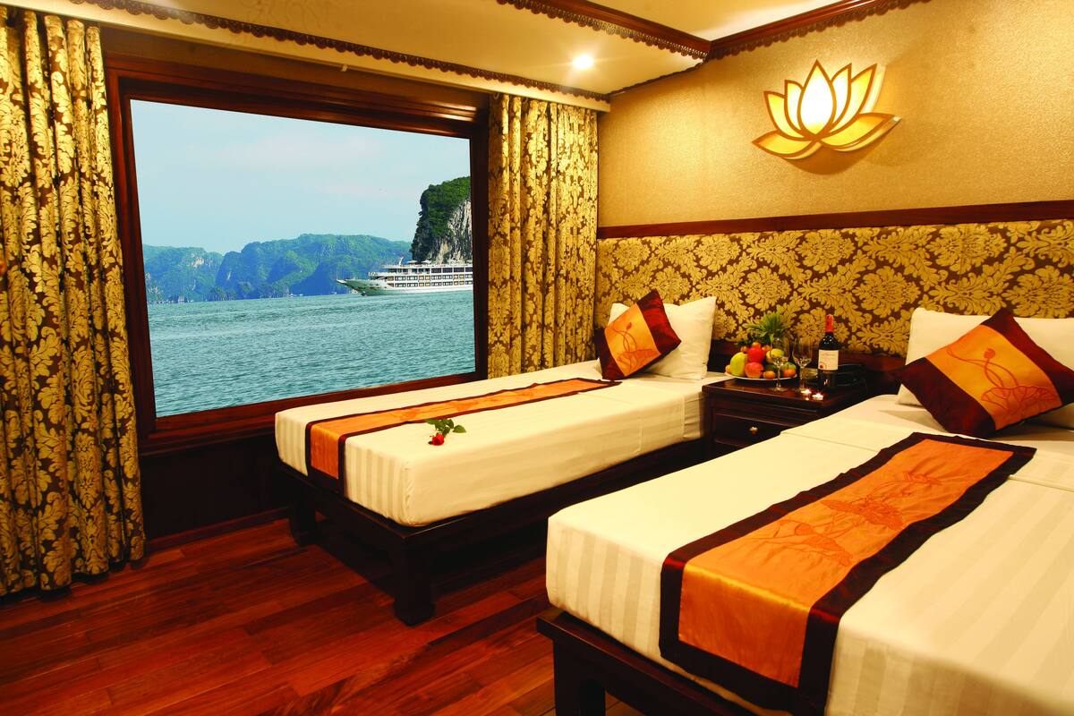 A hotel room with two beds, a large window with curtains, a lotus wall lamp, and a view of a river and mountains.