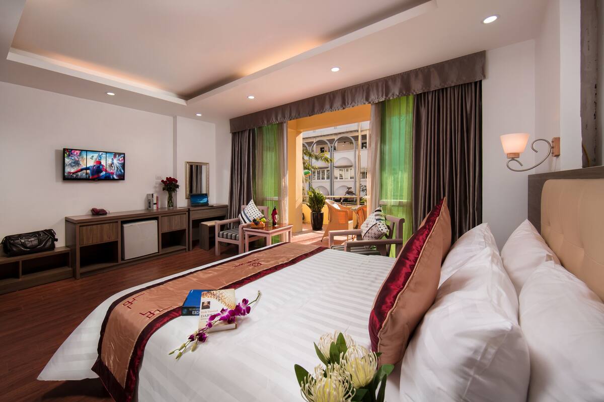 Ein Hotelzimmer mit einem großen Bett, einem Schreibtisch, einem Stuhl und einem Fernseher. Ein Fenster mit Vorhängen bietet einen Blick nach außen.