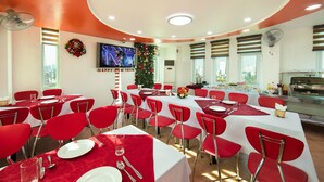 Un comedor con sillas rojas y mesas blancas, un adorno navideño, una pantalla de televisión y un bufé.