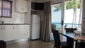 A modern kitchen with white cabinets, a built-in oven, and a dining area with a table and chairs. - Tropical Beach Caravan Park (Bowen)