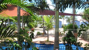A pool surrounded by a fence, with palm trees and a red canopy overhead. - Tropical Beach Caravan Park (Bowen)