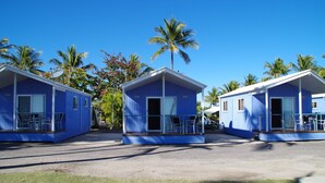 Three blue cabins with glass doors and windows, each with a small porch and chairs. - Tropical Beach Caravan Park (Bowen)