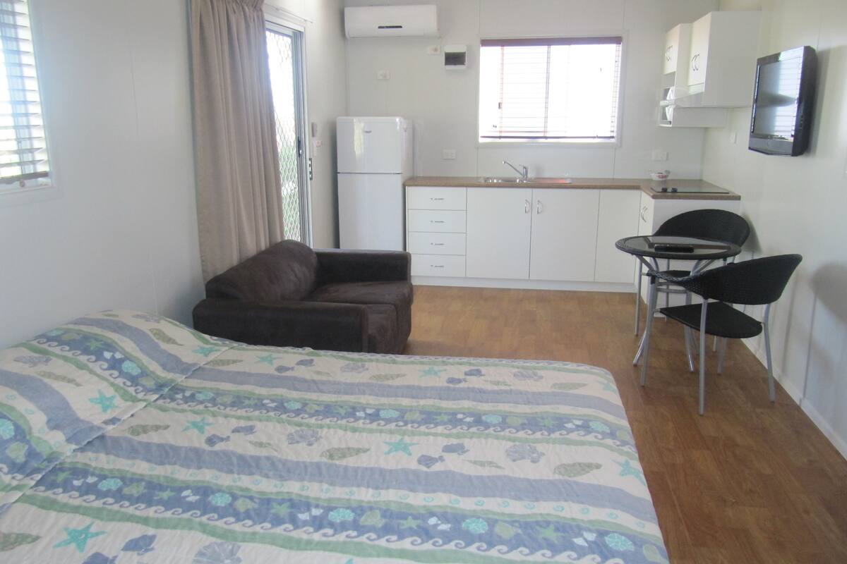 Un dormitorio con cama, un sofá pequeño, un comedor con mesa y sillas, y una cocina con armarios y un refrigerador.