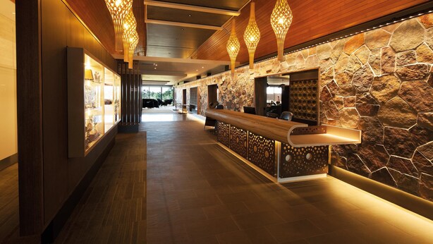Un vestíbulo moderno con mostrador de recepción, paneles de madera, pared de piedra y lámparas colgantes.