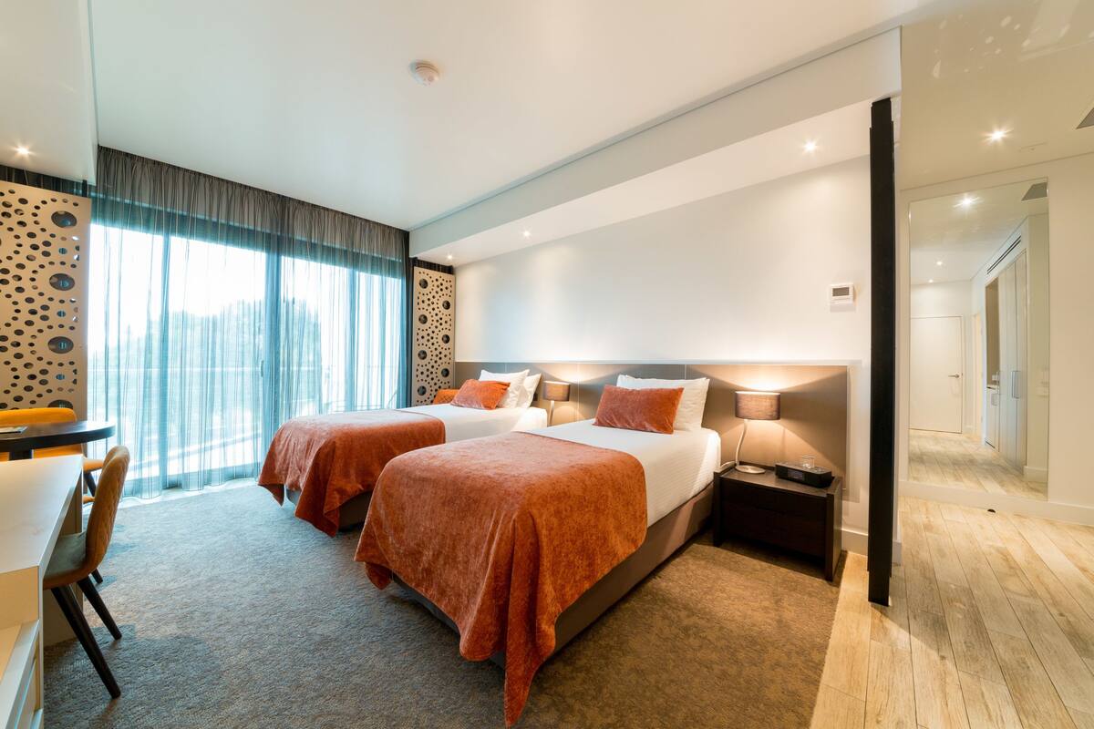 A hotel room with two beds, a desk, and a chair.