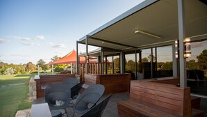 Un patio al aire libre con bancos y sillas de madera, una zona de estar techada y vistas a un campo de golf.