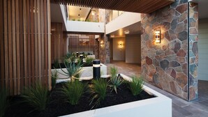 Un edificio moderno con fachada de piedra, techo de listones de madera y un jardín ajardinado con plantas y una jardinera blanca.