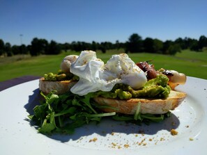 Un plat amb un ou escalfat, advocat i verdures sobre torrat, amb un camp de golf al fons.