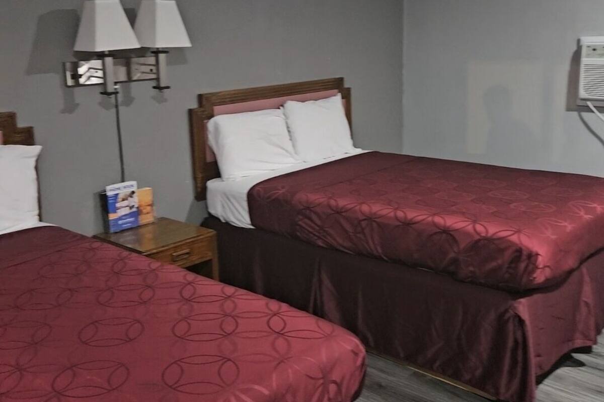 Une chambre d’hôtel avec deux lits simples, une table de chevet avec une lampe et un climatiseur fixé au mur.