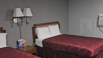 A hotel room with two single beds, a nightstand with a lamp, and a wall-mounted air conditioner.