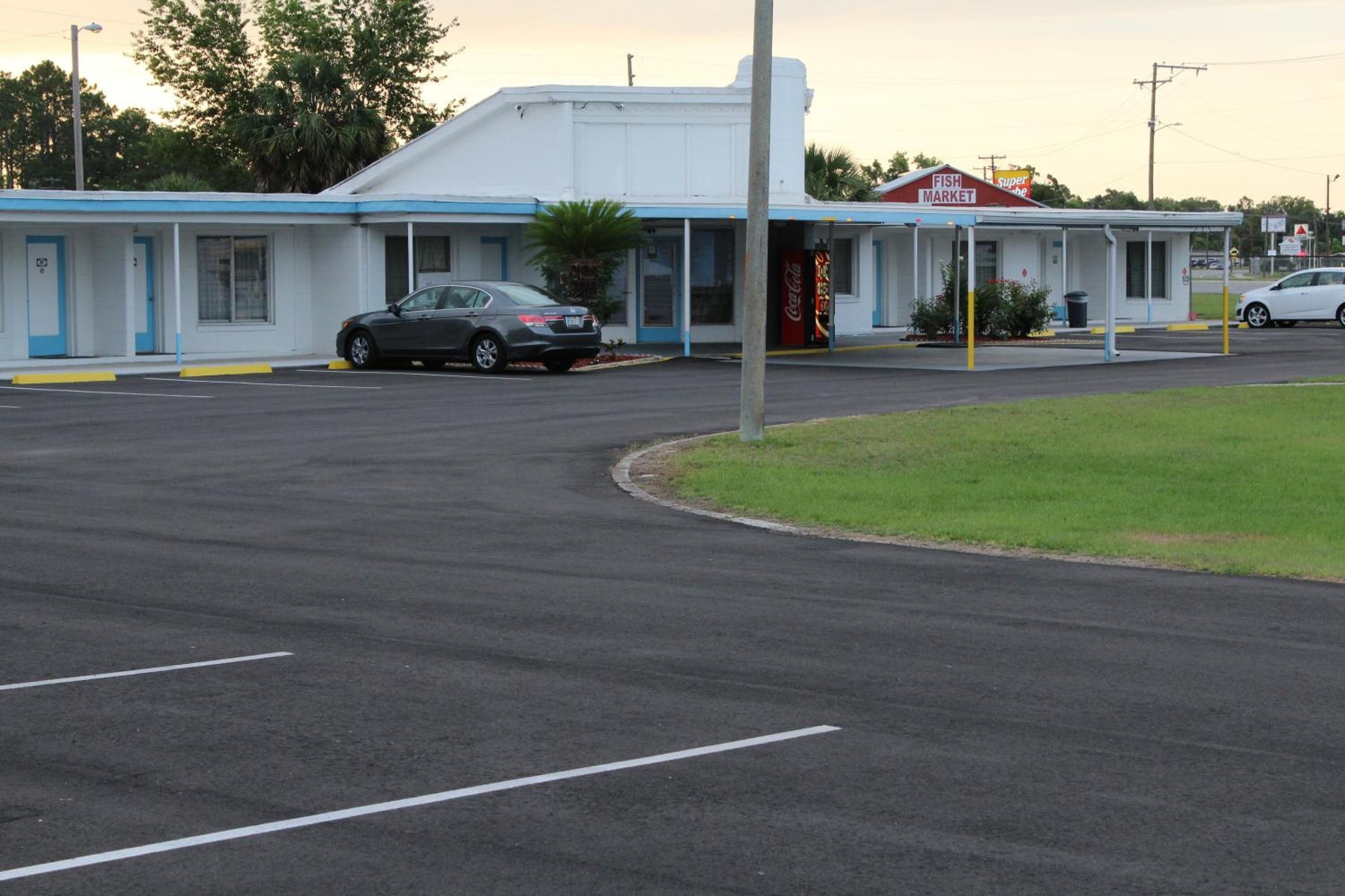 Un motel composé d’un bâtiment d’un seul étage, d’un espace de stationnement couvert et d’une enseigne Coca-Cola.