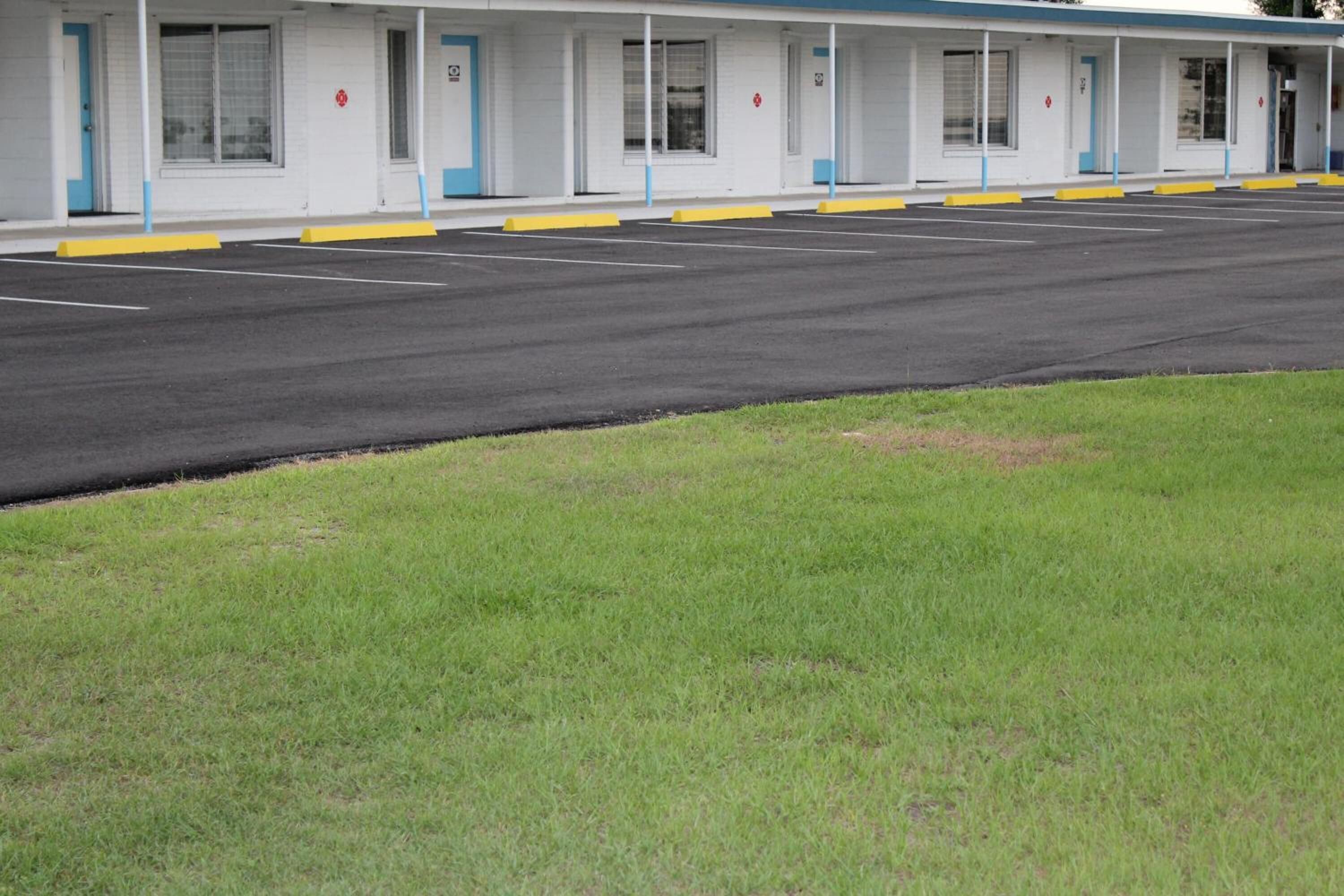Um motel com uma fileira de quartos, cada um com porta e janelas. Há um estacionamento em frente ao motel.