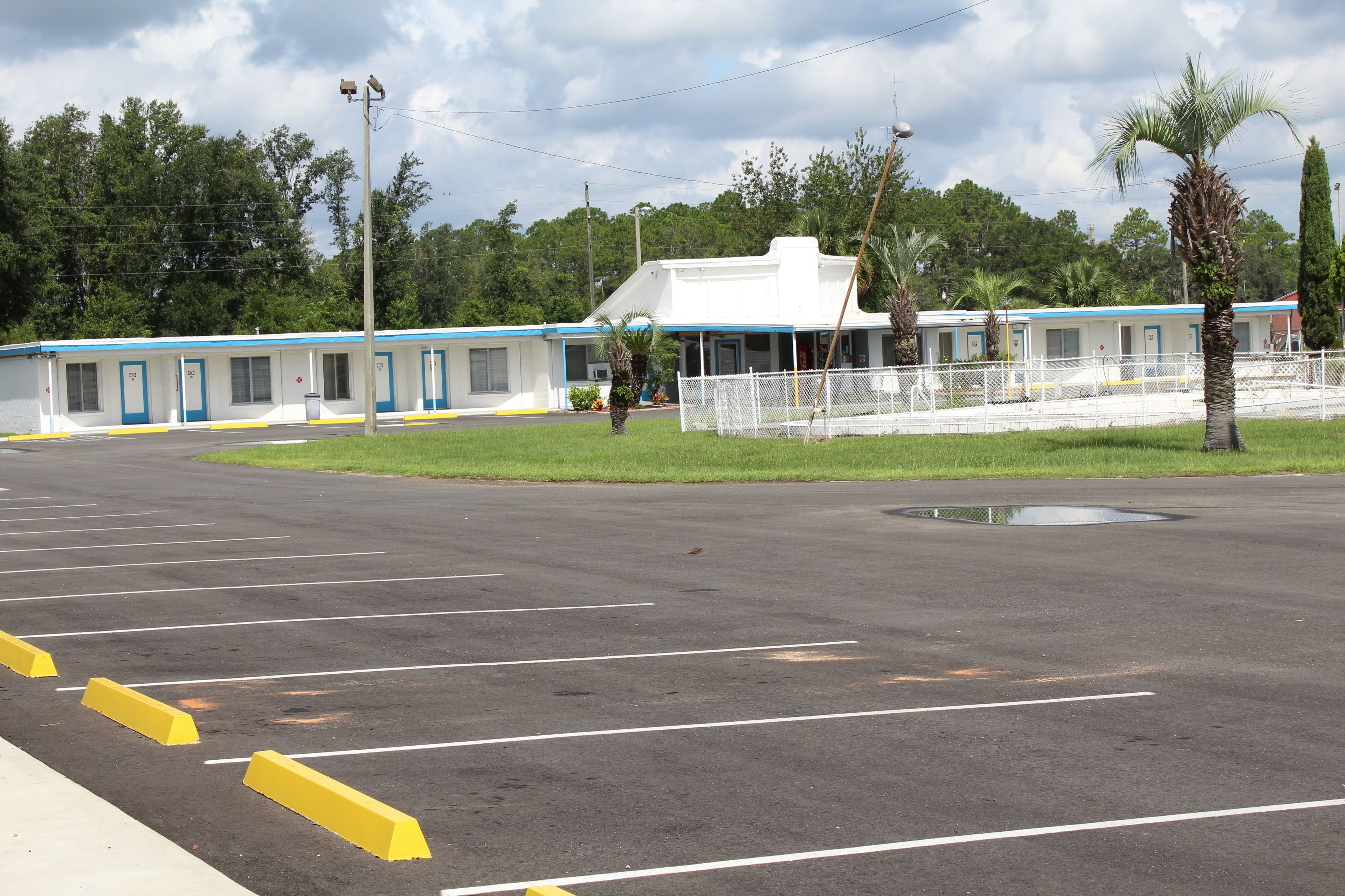 A motel with a row of rooms, a fenced parking area, and a palm tree.