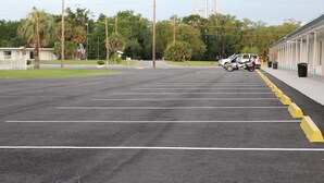 A parking lot with marked spaces, a building with a covered walkway, and a few parked vehicles.