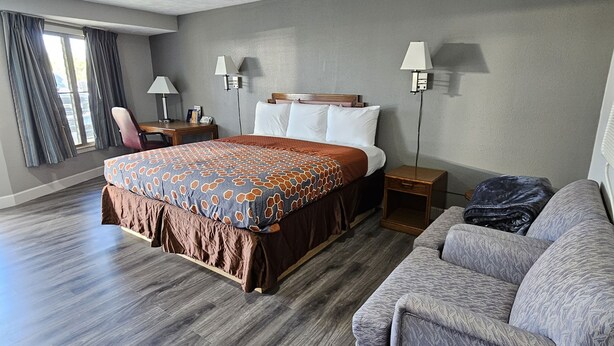 A hotel room with a large bed, a sofa, a desk, and a lamp.