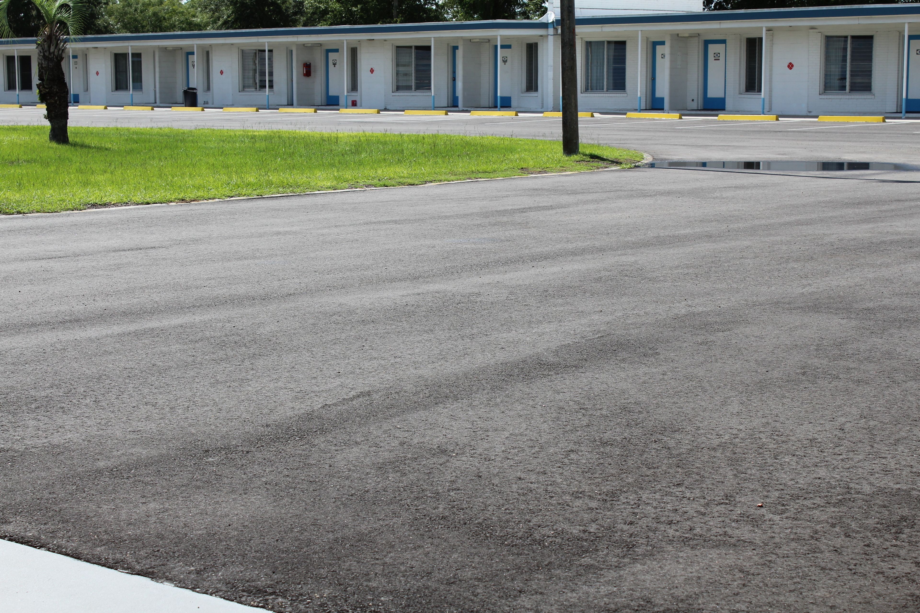 A motel with a row of rooms, a grassy area, and a wet parking lot.