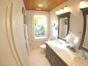 A bathroom with a large window, a vanity with a mirror, and a toilet. - The Hibiscus House  (Fort Myers)