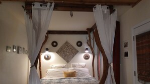 A bed with a patterned bedspread, a canopy, and wall-mounted lights. - Aloha Crater Lodge (Volcano)