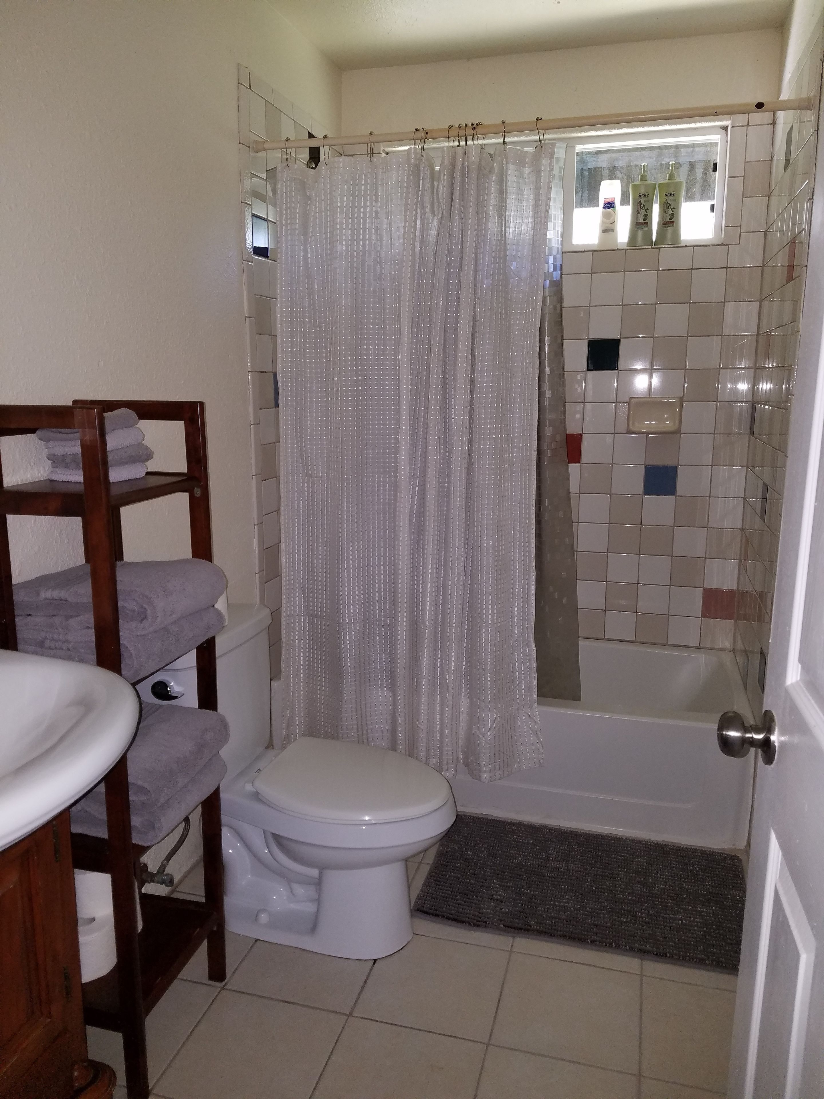 Un bagno con il water, uno scaffale in legno con asciugamani, una tenda da doccia e un rivestimento in piastrelle.