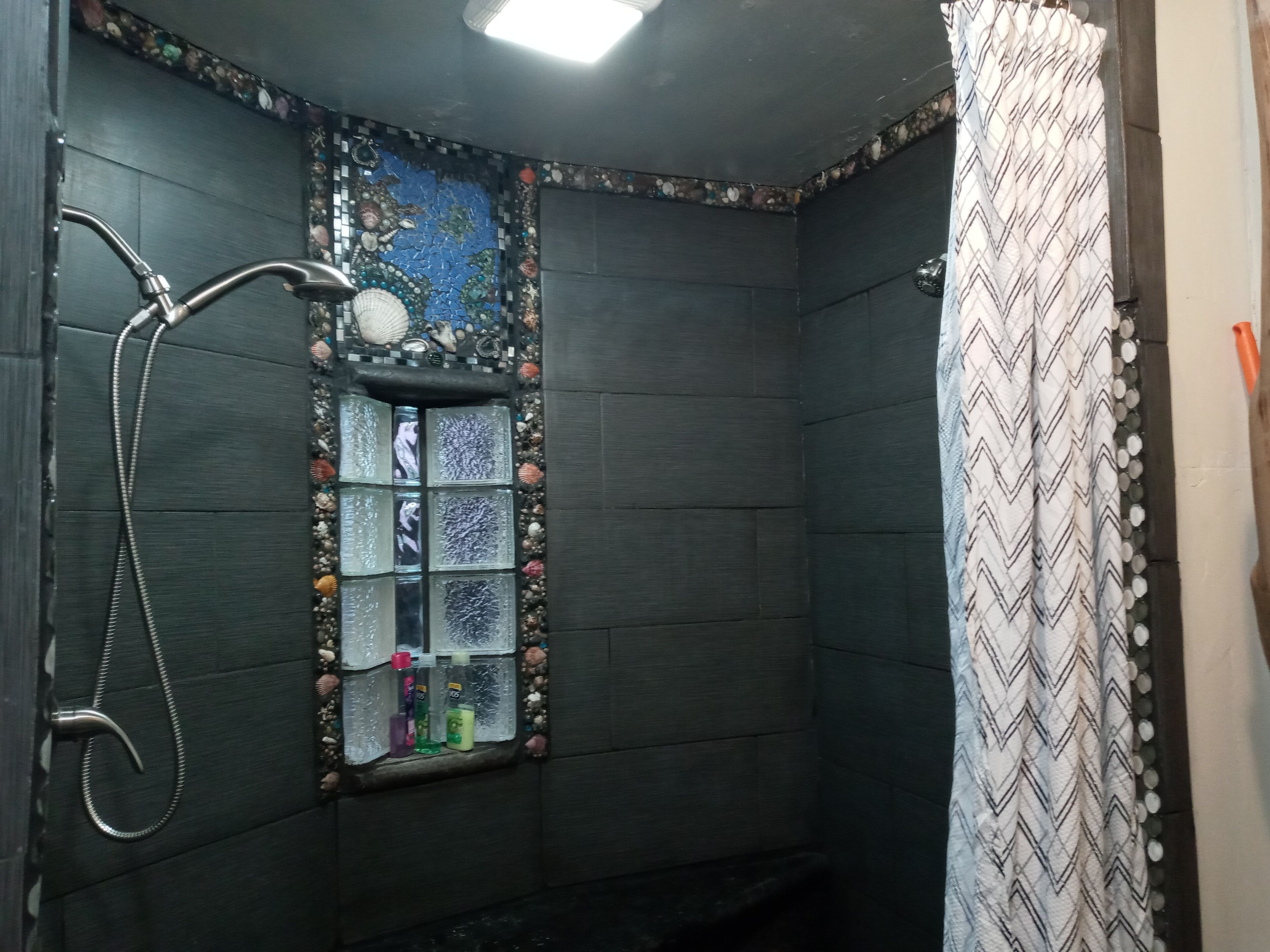 Un baño con ducha, una ventana con azulejos decorativos y una cortina de estampado en zigzag.