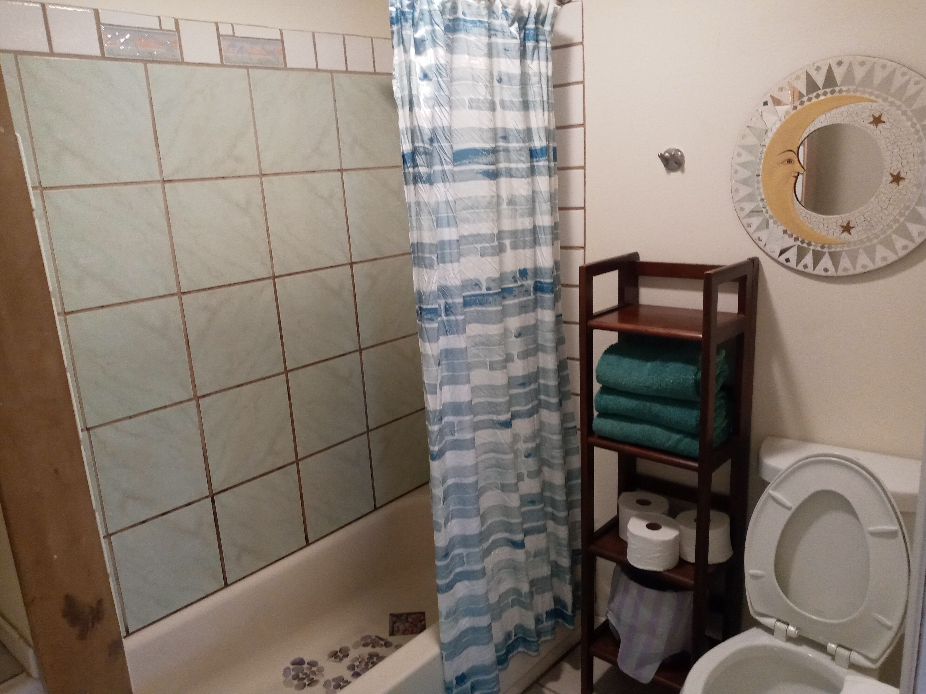A bathroom with a shower, a toilet, and a shelf with towels and toilet paper.