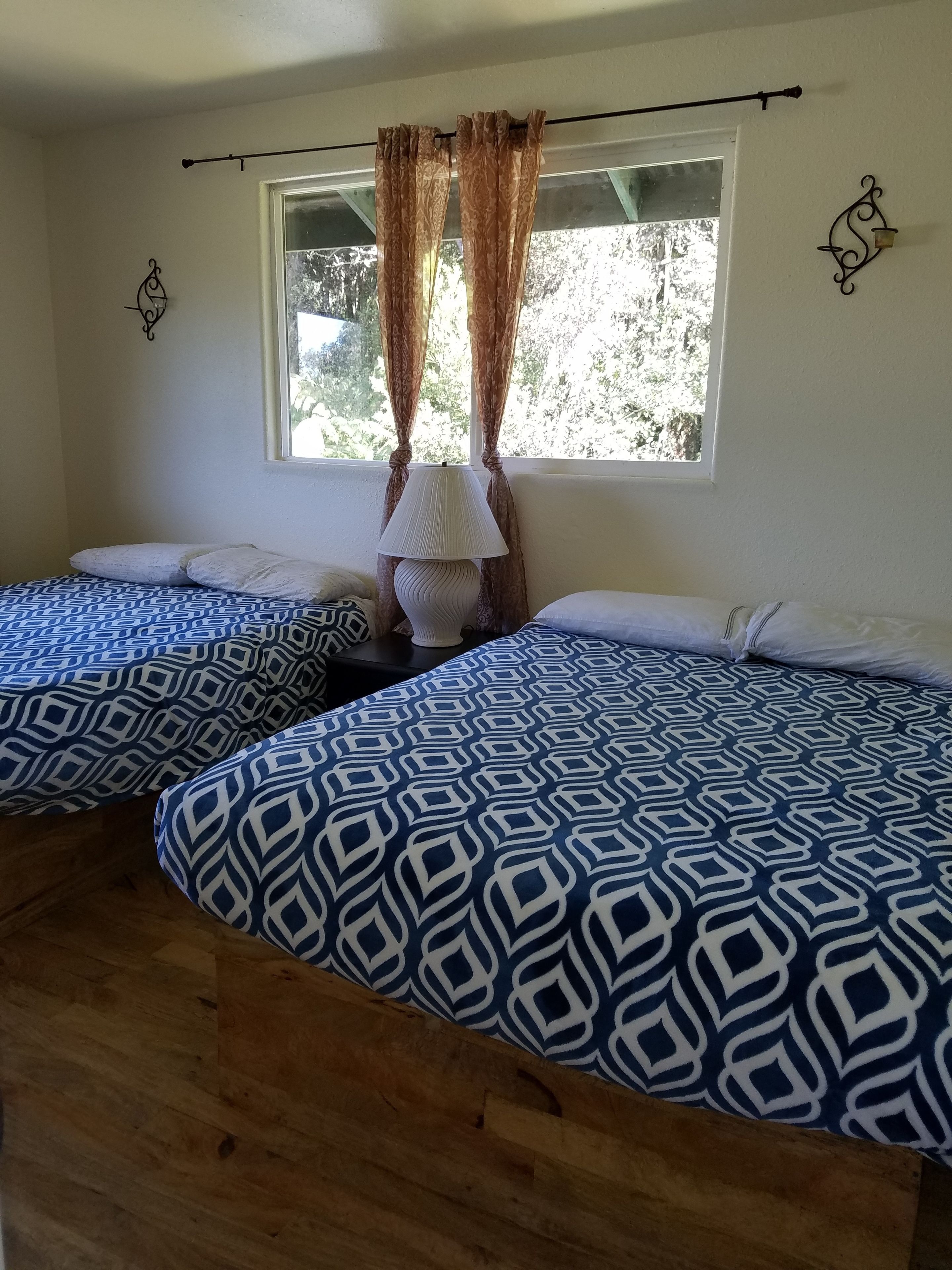 A room with two beds, a window with curtains, a lamp, and wall decorations.