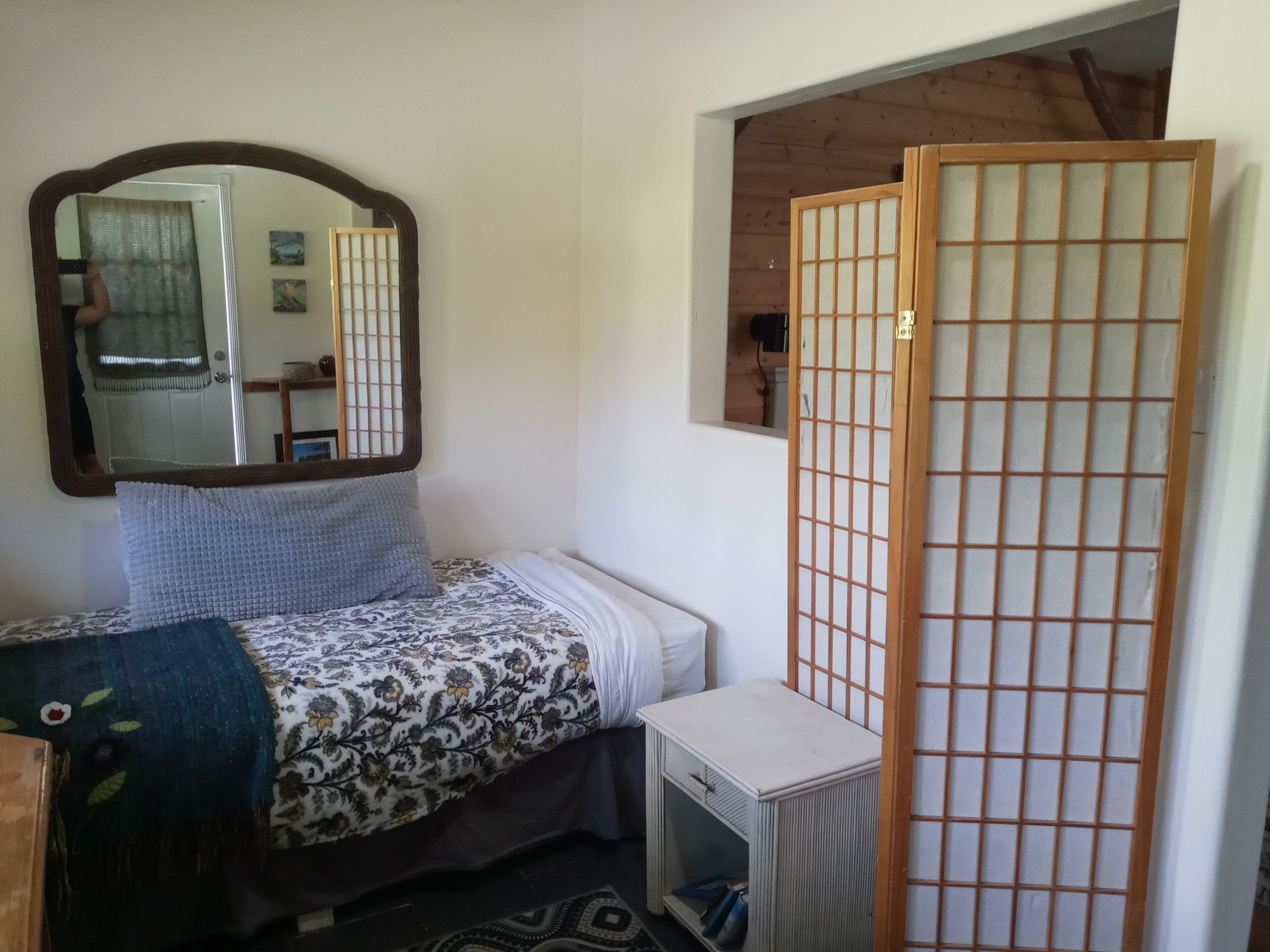 A small, compact room with a bed, a bedside table, a mirror, and a sliding shoji screen.