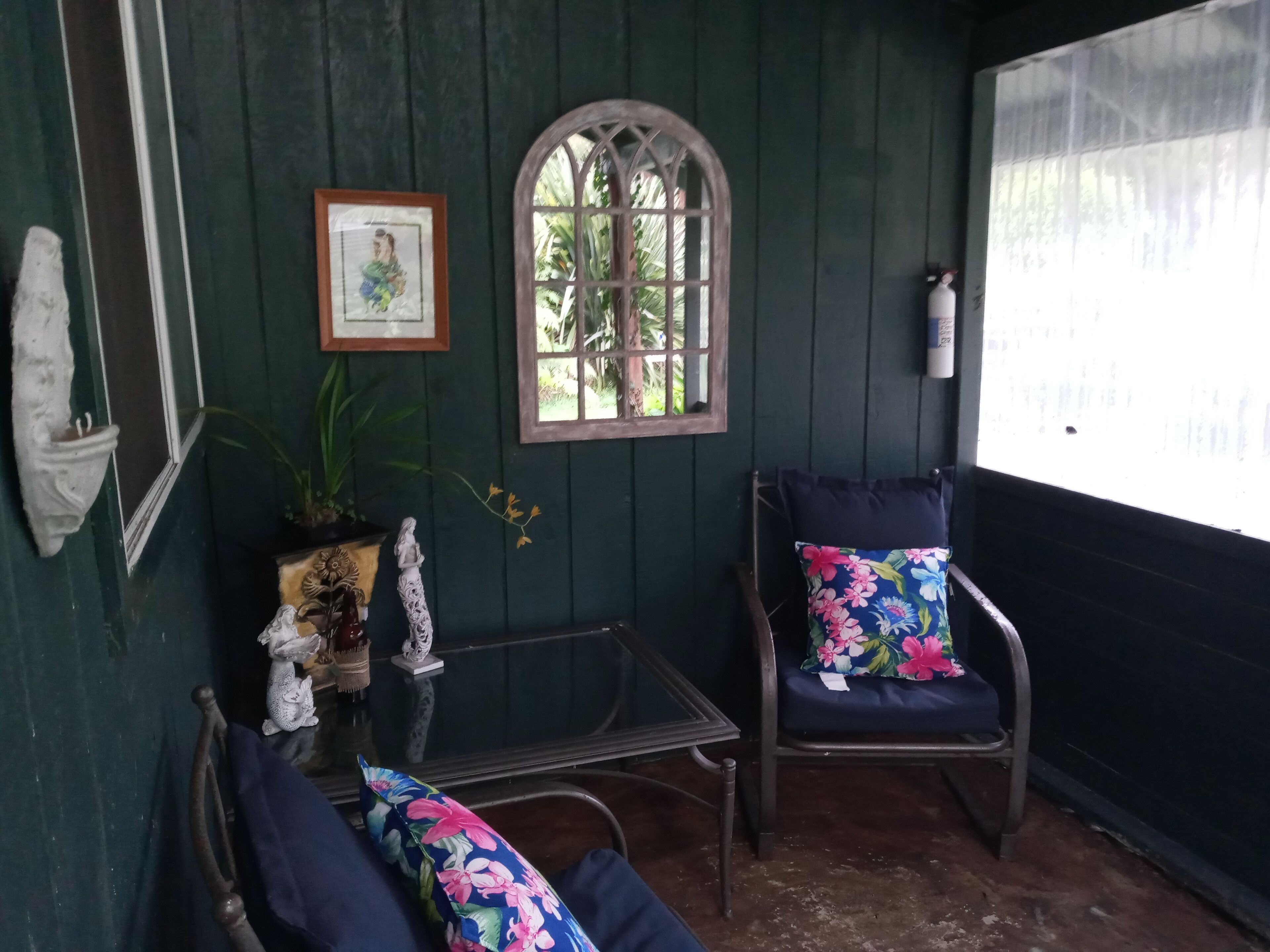 Um quarto acolhedor com um banco de madeira, uma cadeira com almofada floral, uma mesa pequena e uma janela com vista para o verde.